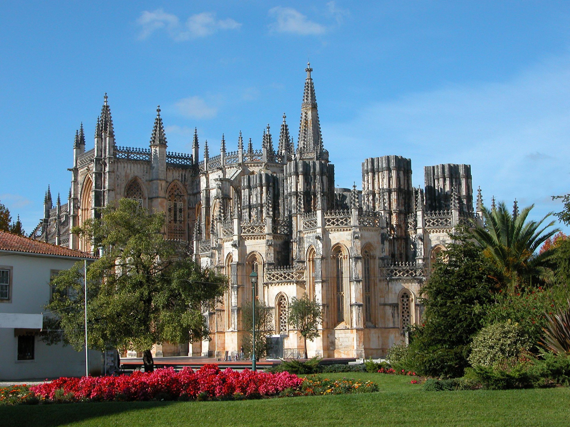 Gothic cathedral with ornate spires and lush gardens under a blue sky.