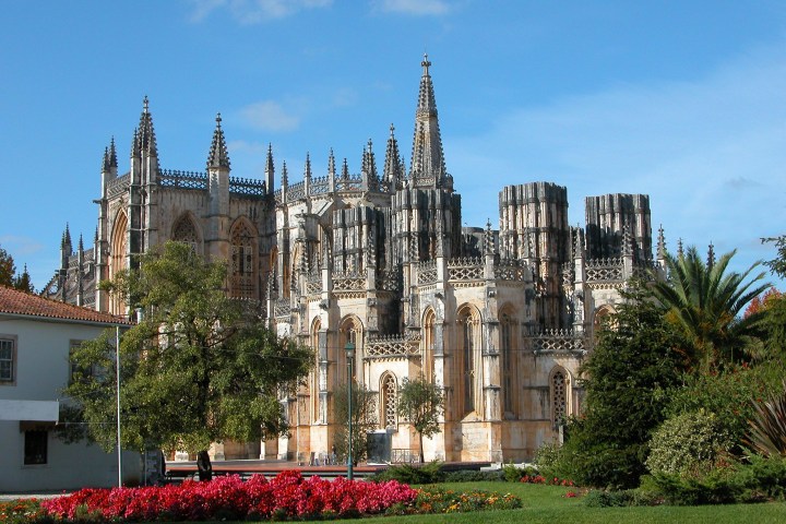Gothic cathedral with ornate spires and lush gardens under a blue sky.