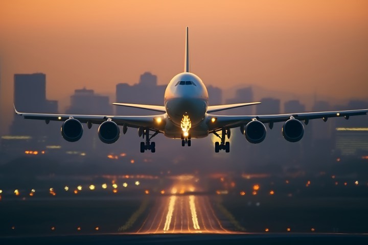 Airplane landing on runway at sunset with city skyline in background.