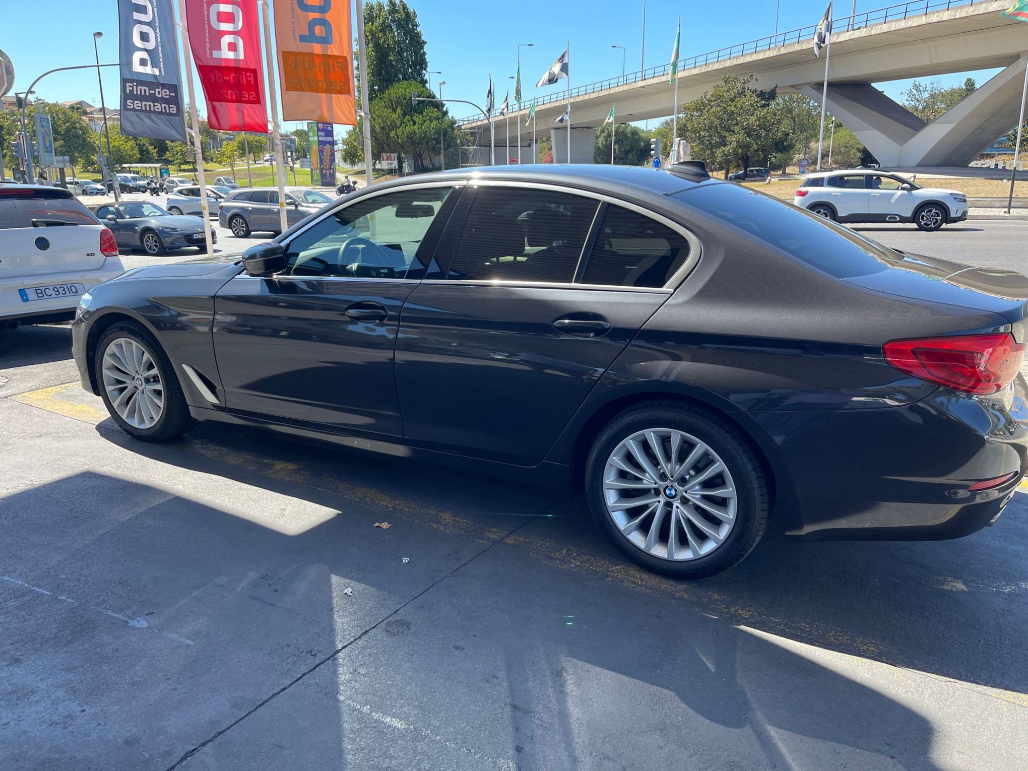 Side view of a parked black sedan near a roadway with colorful flags.