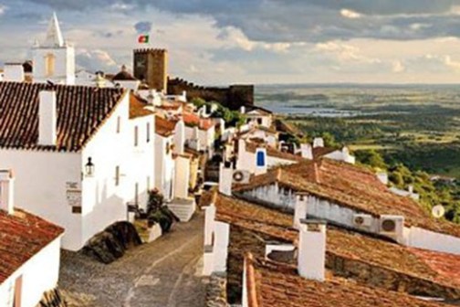 Person walking on a narrow cobblestone street in a village with white houses and red roofs.