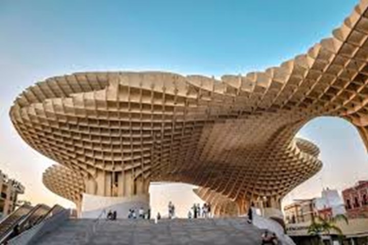 Large wooden lattice structure with people standing below against a blue sky.
