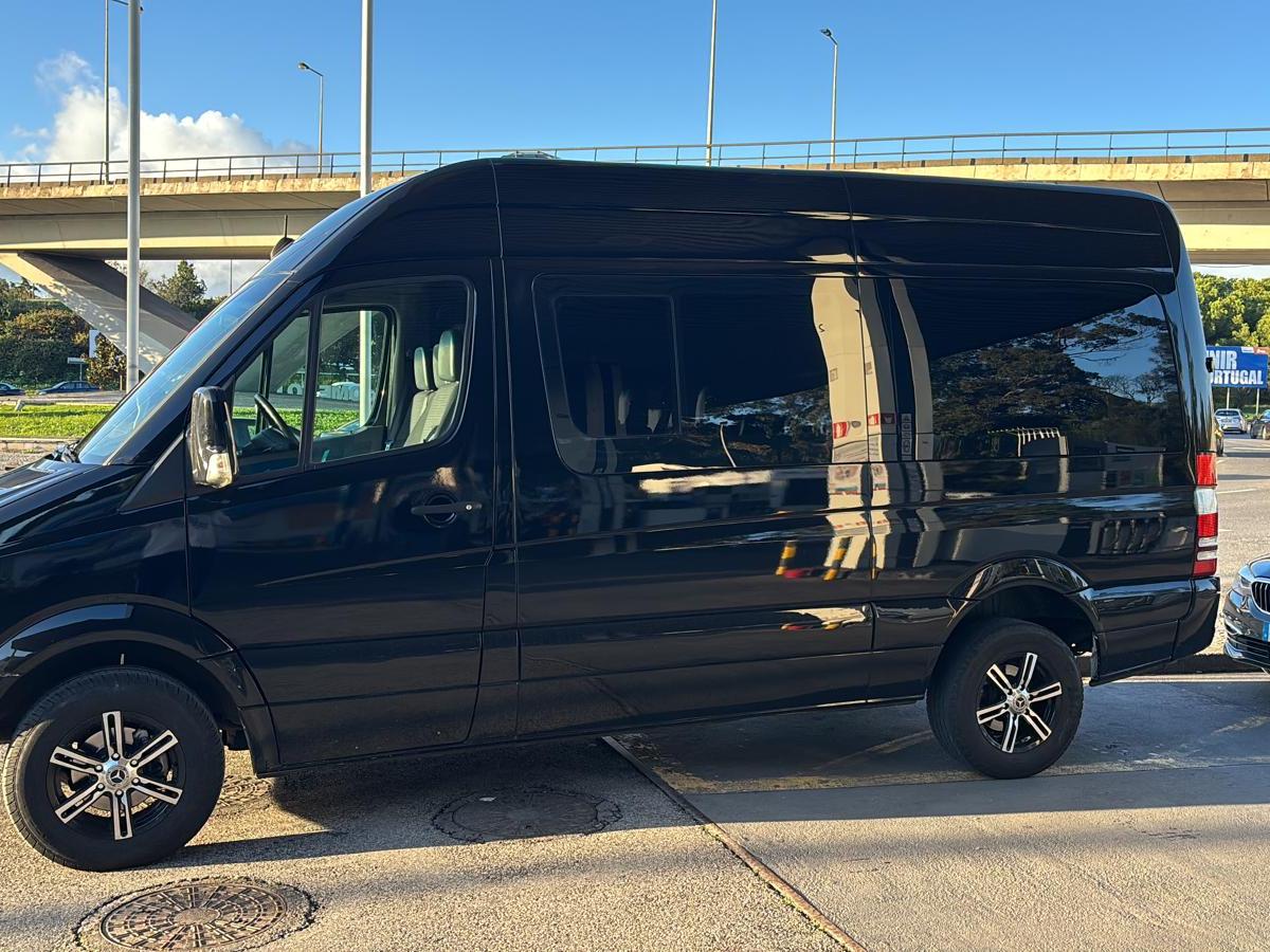 Black van parked next to a black car on a sunny day near an overpass.