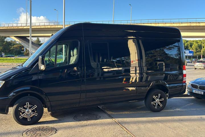 Black van parked next to a black car on a sunny day near an overpass.
