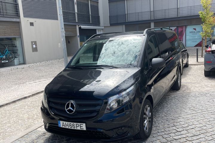 Black van parked on cobblestone street between modern buildings.