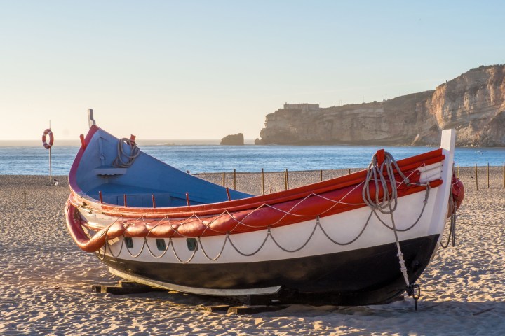 Colorful boat on sandy beach with cliffs in background at sunset.