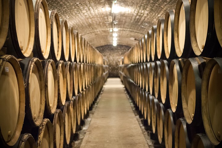 A cellar with rows of wooden barrels on either side under a brick archway ceiling.