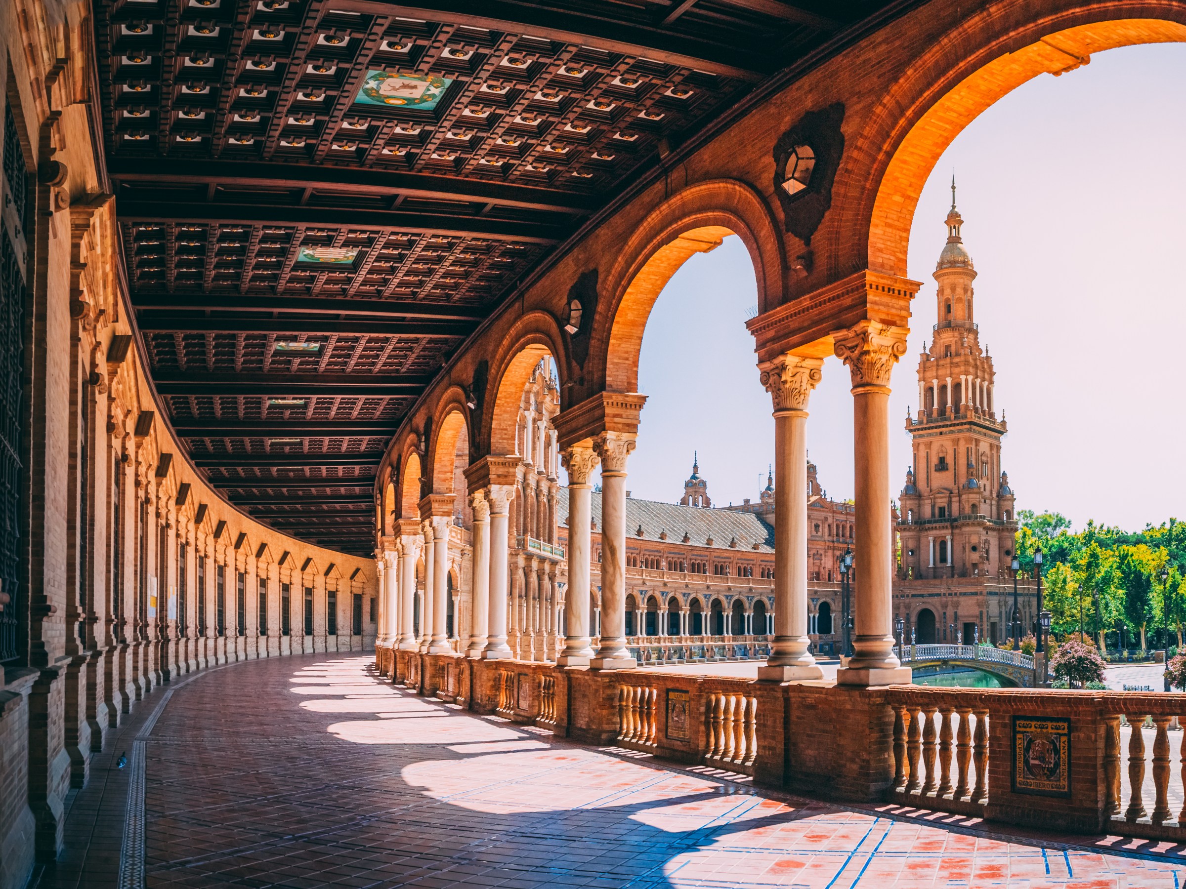 Arched corridor with view of plaza and ornate tower in sunny weather.