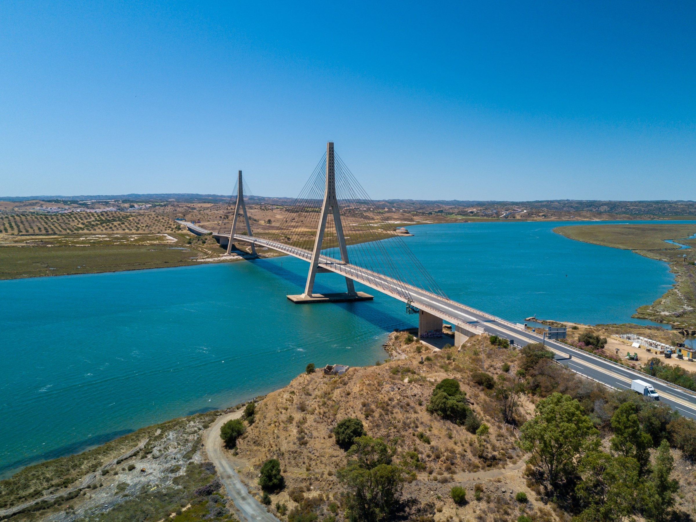 Cable-stayed bridge over a wide blue river in a rural landscape under a clear blue sky.