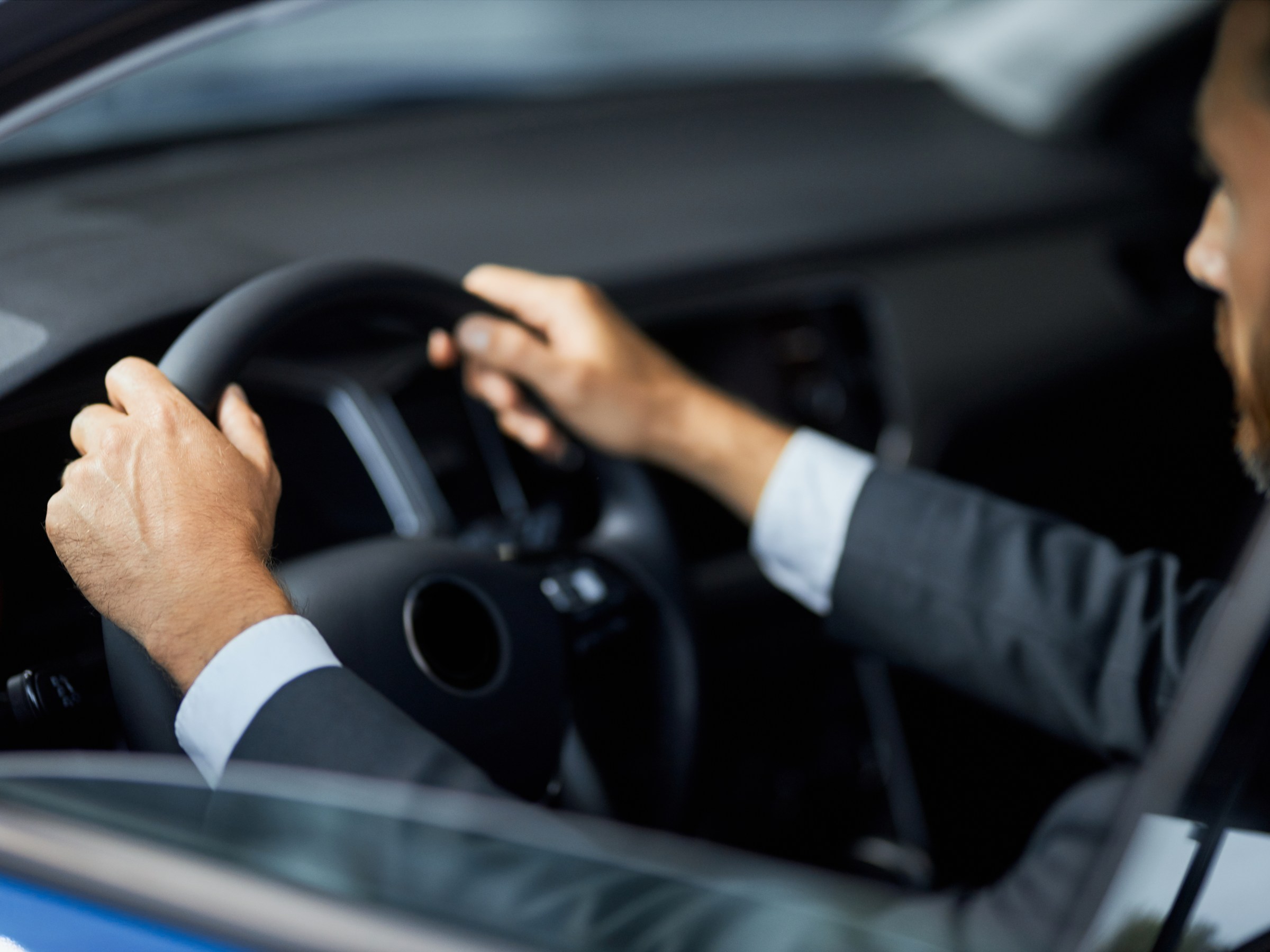 Man in suit driving a car, focused on steering wheel.