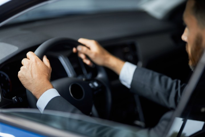 Man in suit driving a car, focused on steering wheel.