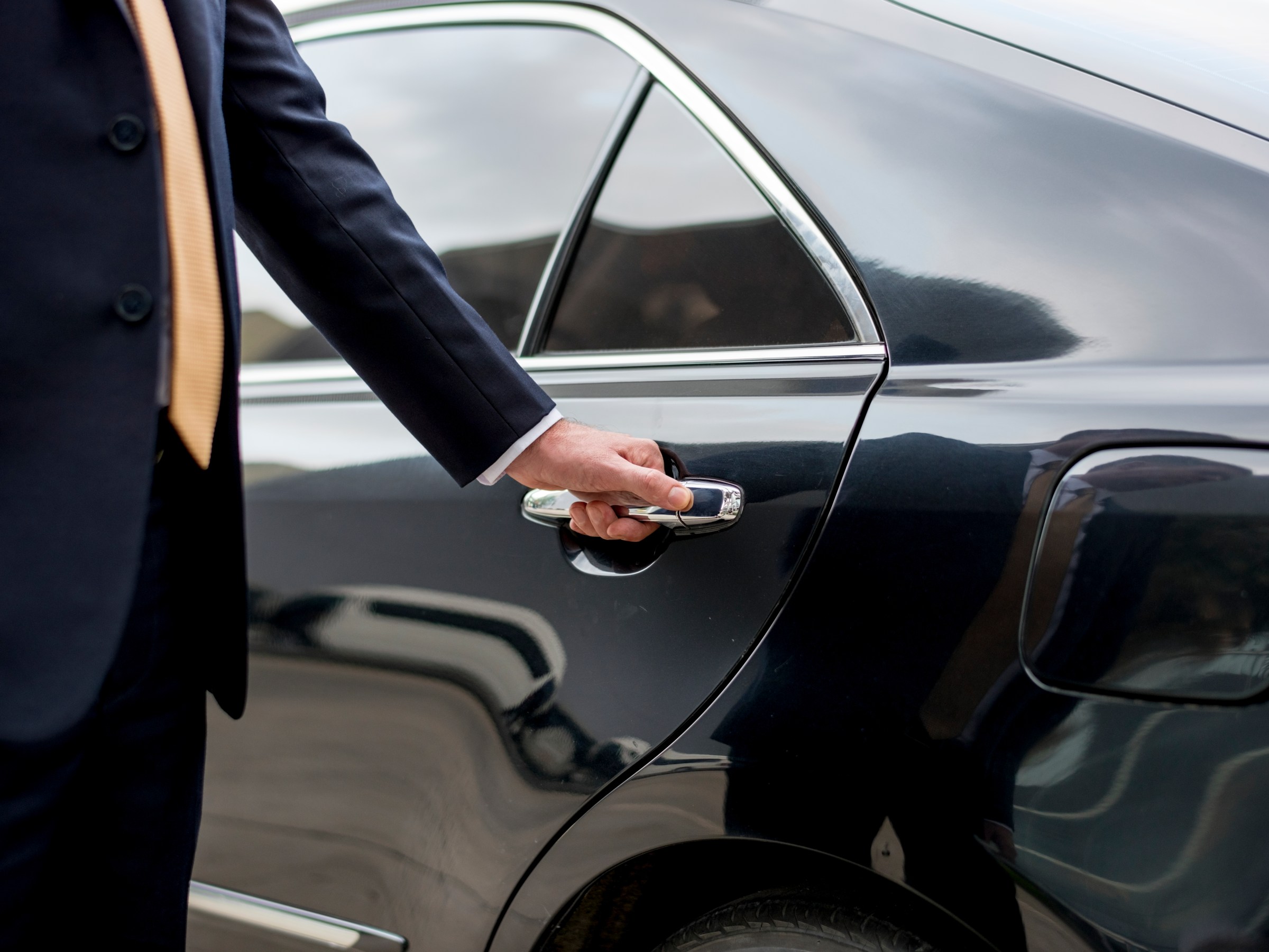 Man in suit opening car door with right hand.