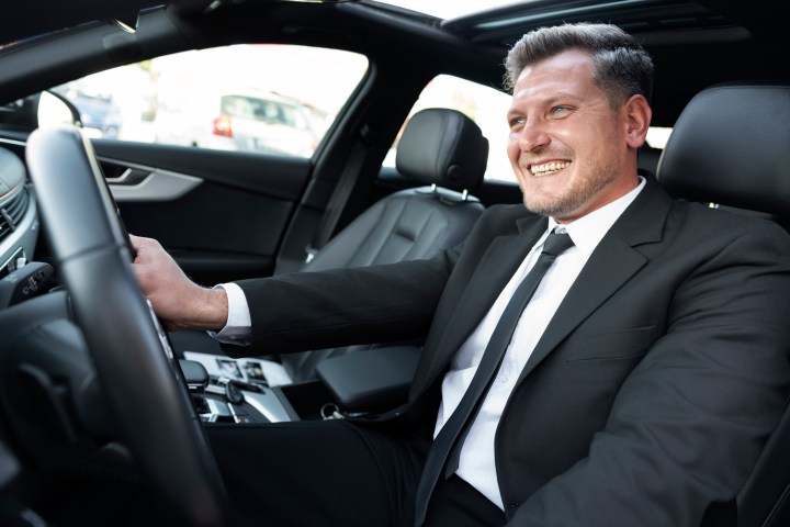 Smiling man in a suit driving a car.
