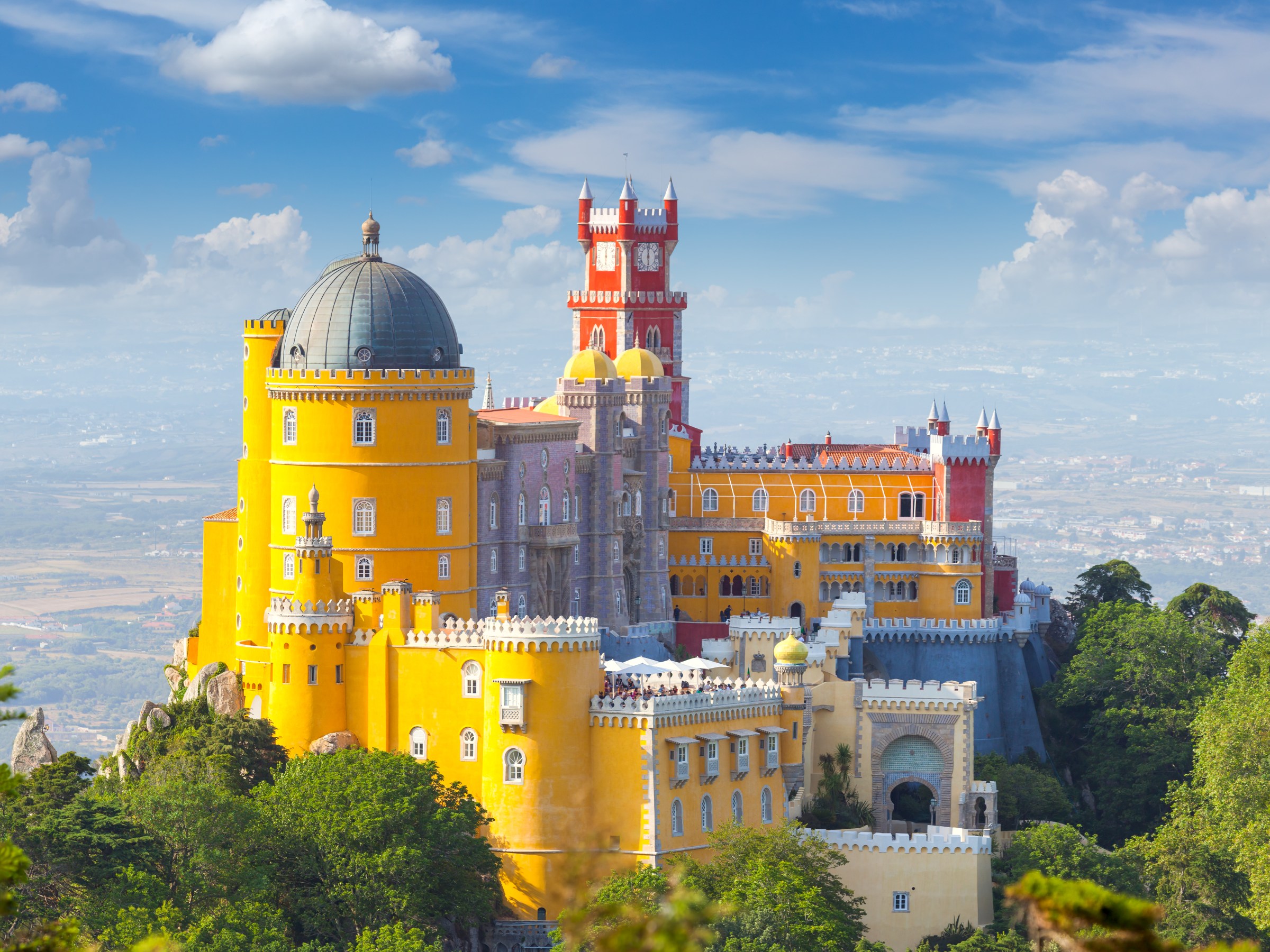 Colorful castle with domes and towers on a hilltop under a blue sky with clouds.