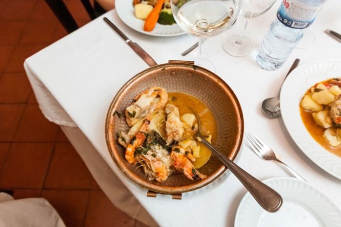 Dish with seafood and sauce on a table with white tablecloth and utensils.