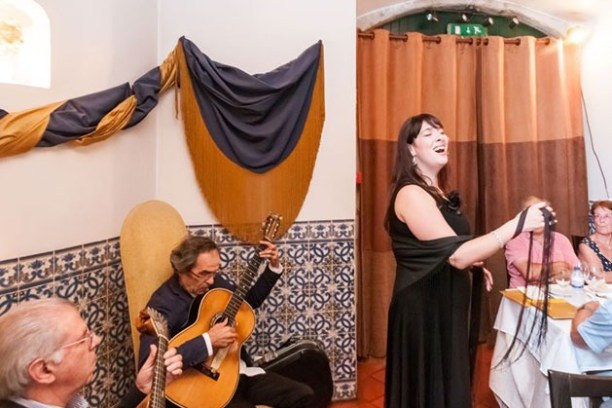 Woman singing with guitarist and audience in a decorated room.