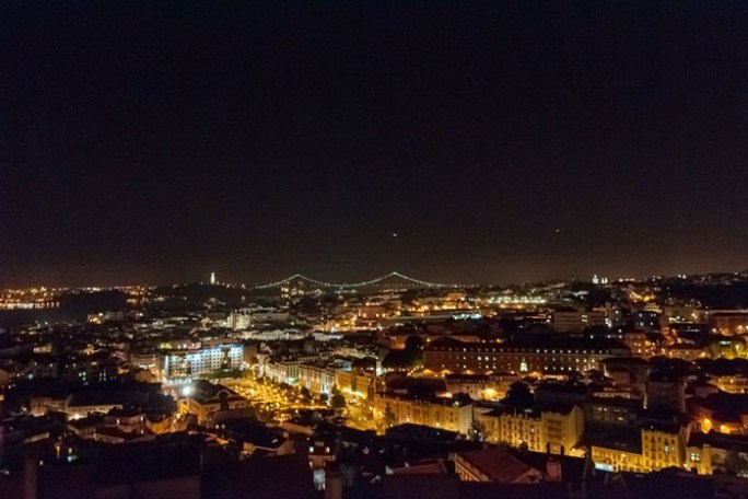 Night cityscape with illuminated buildings and bridge under a dark sky.