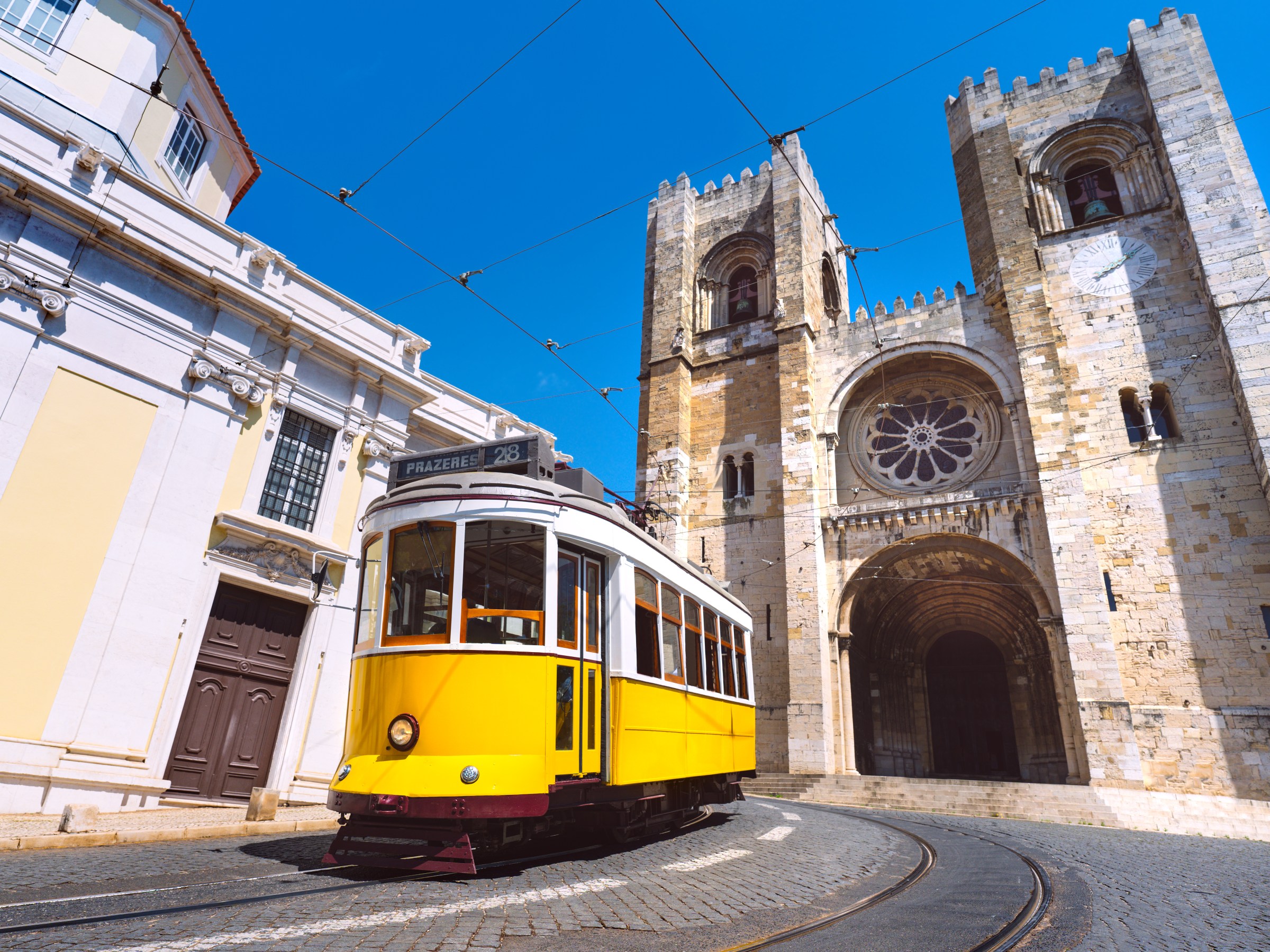 Yellow tram passing historic stone cathedral under a clear blue sky.