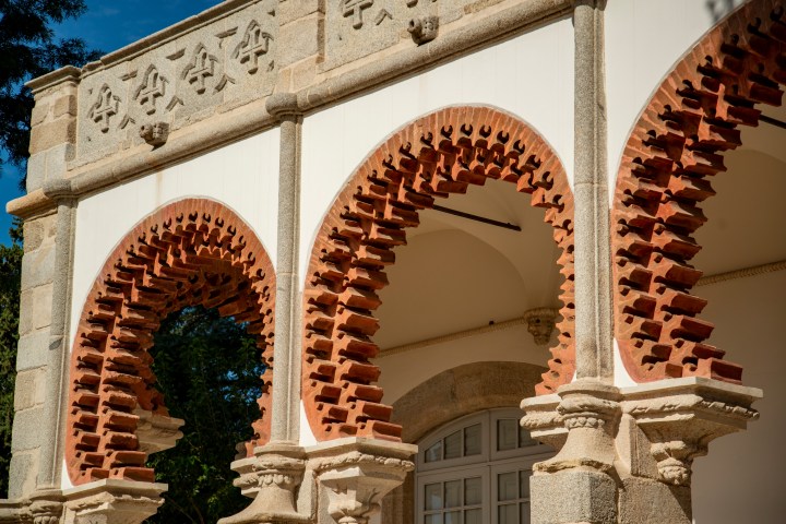 Red brick Moorish-style arches with intricate stone carvings in a sunny outdoor setting.