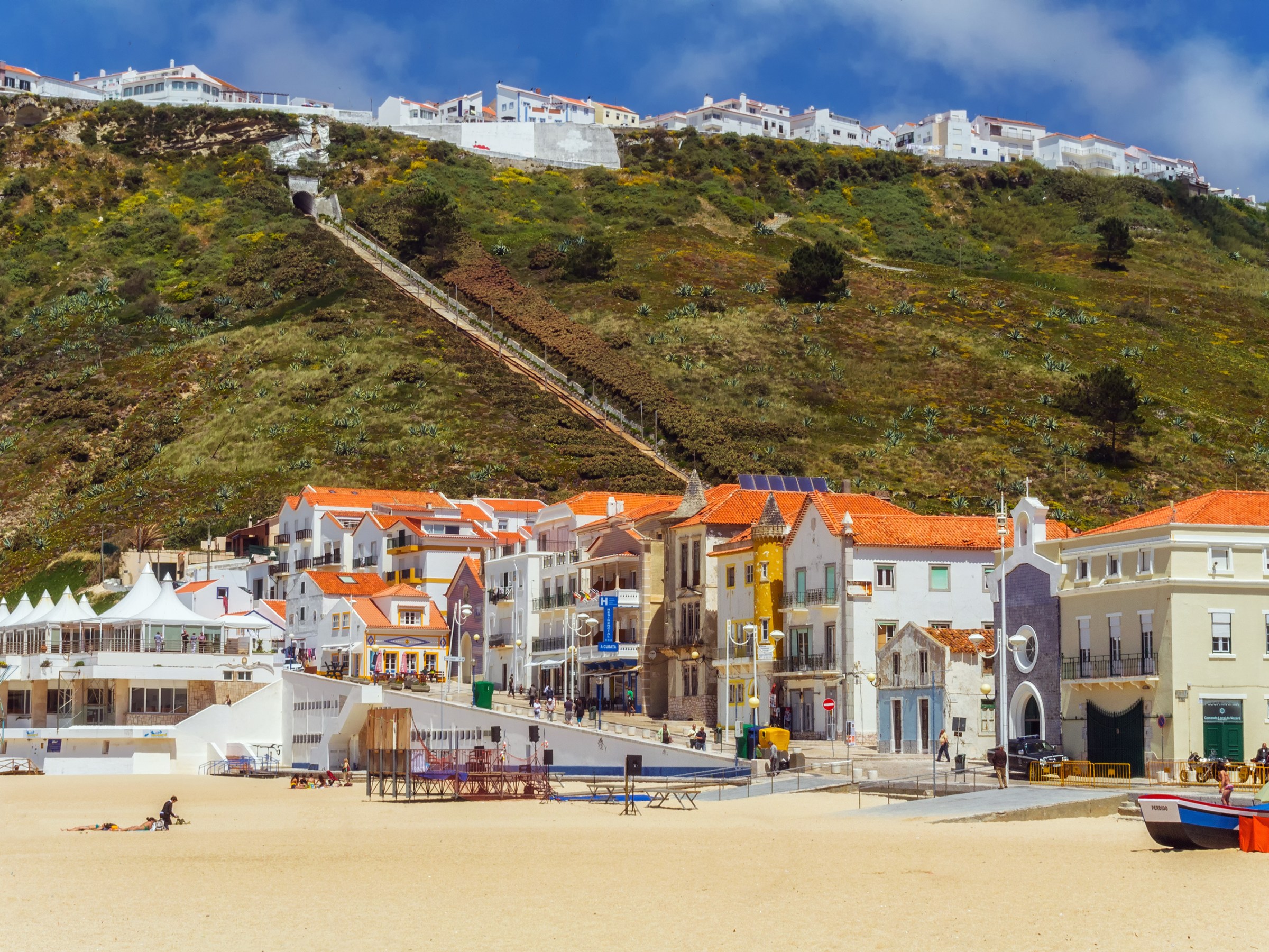 Beachfront village with colorful rooftops and hillside in the background under a blue sky.