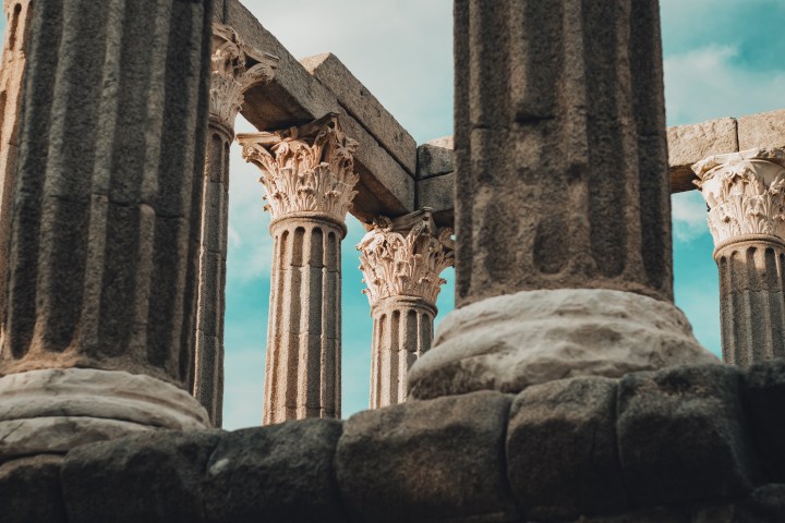 View of ancient stone columns with ornate capitals under a blue sky.
