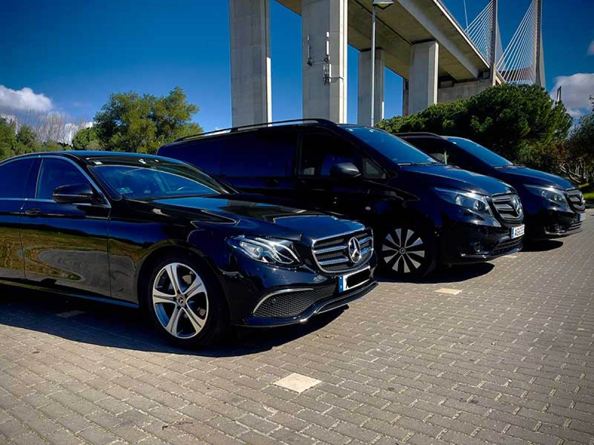 Three black Mercedes vehicles parked under a bridge on a sunny day.