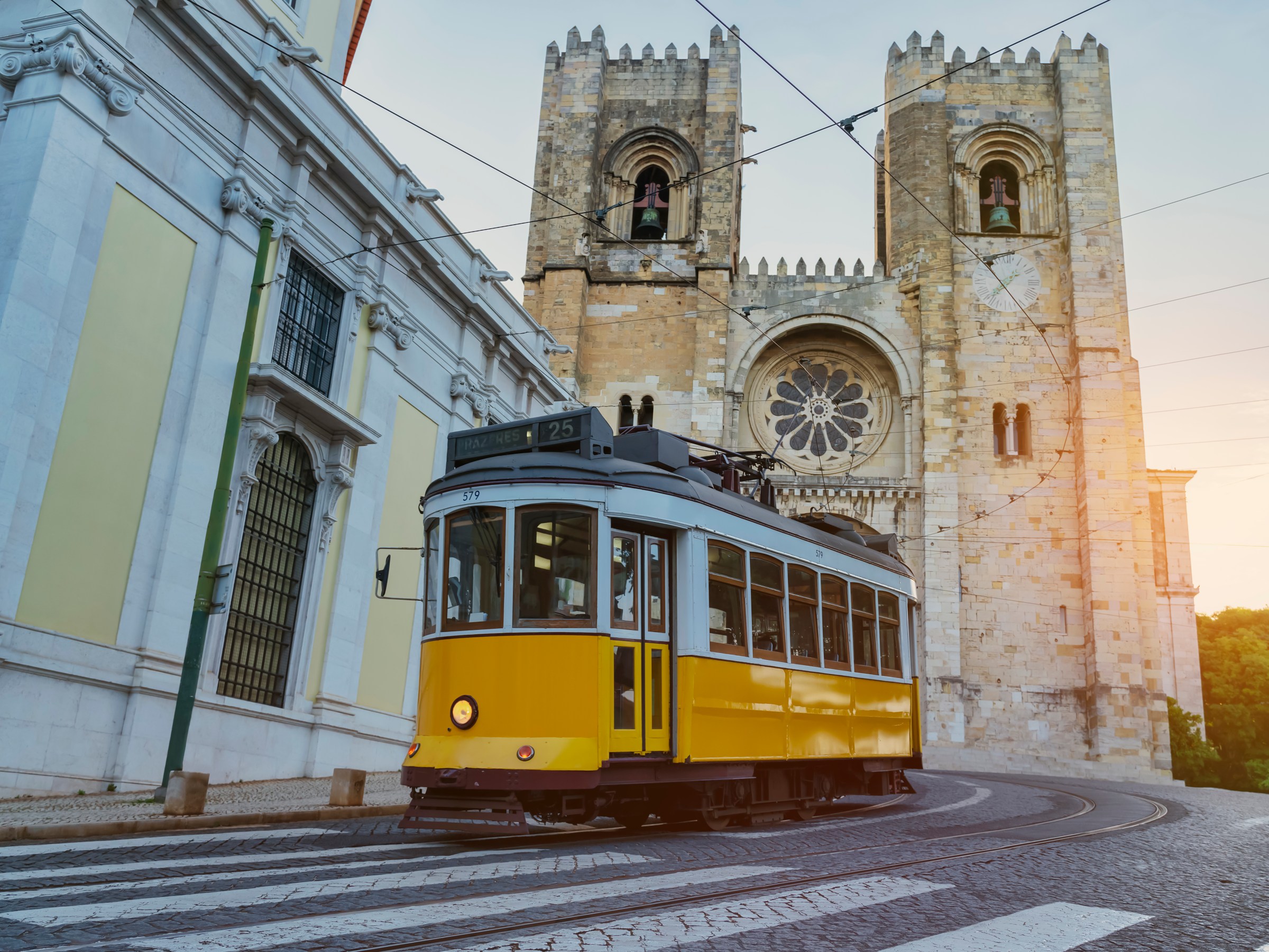 Yellow tram passing by a historic cathedral with two bell towers at sunset.