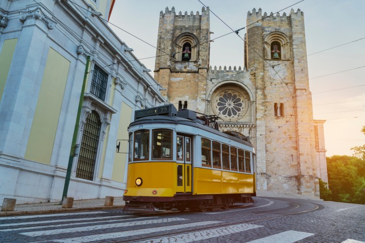 Yellow tram passing by a historic cathedral with two bell towers at sunset.