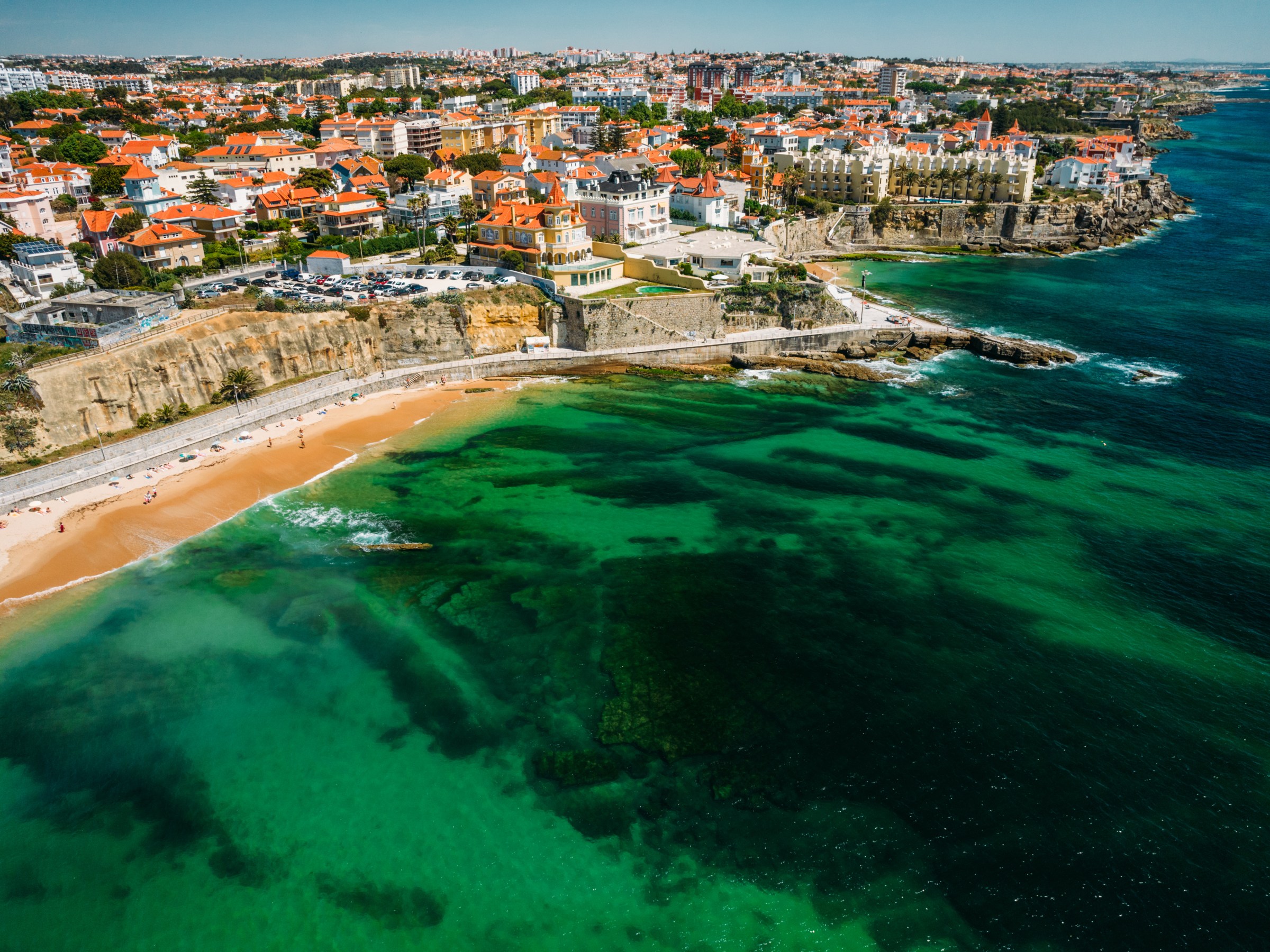 Aerial view of a coastal town with red-roofed buildings and a sandy beach.