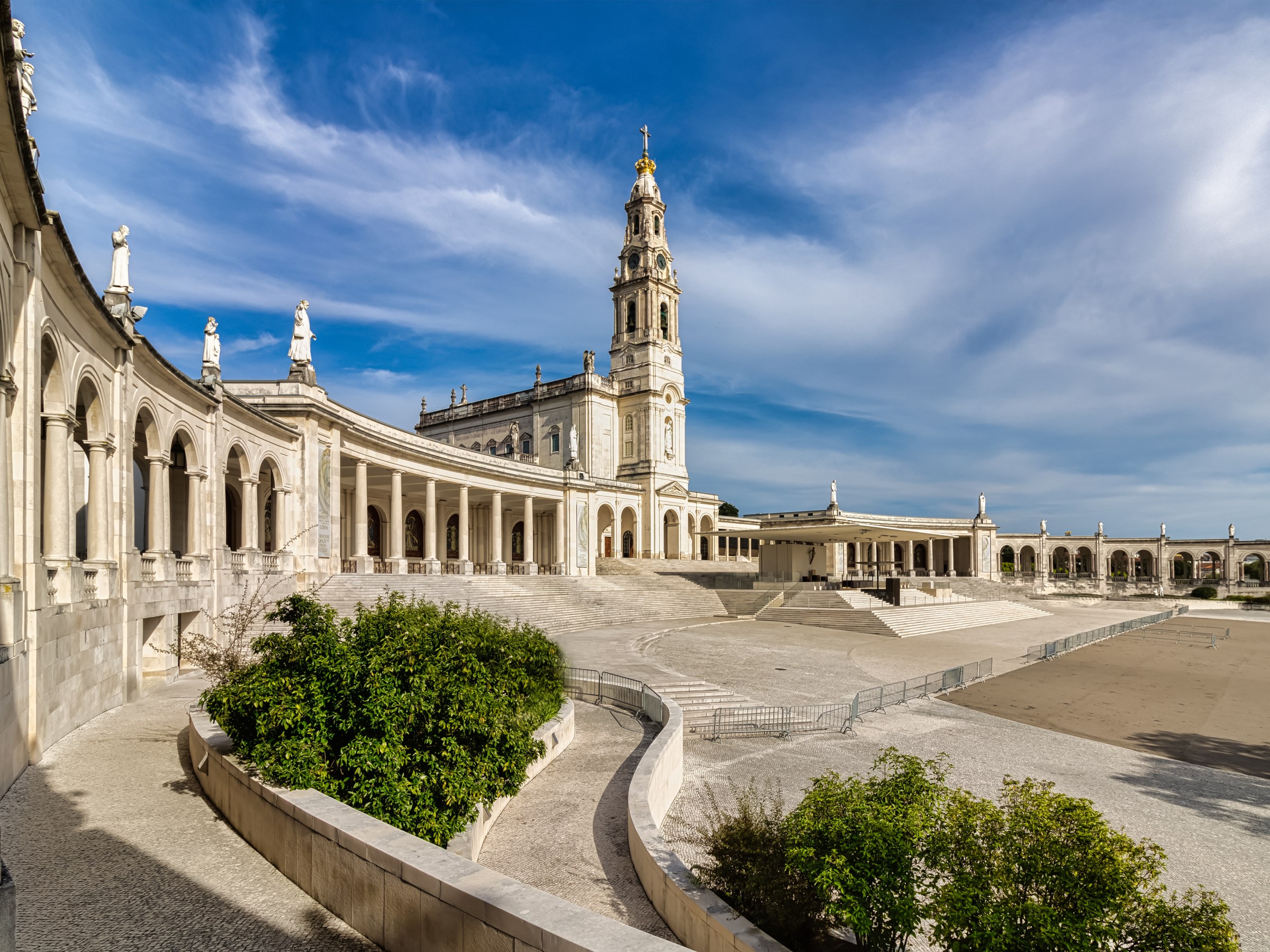 Large neoclassical building with arches and a tall bell tower under a blue sky.