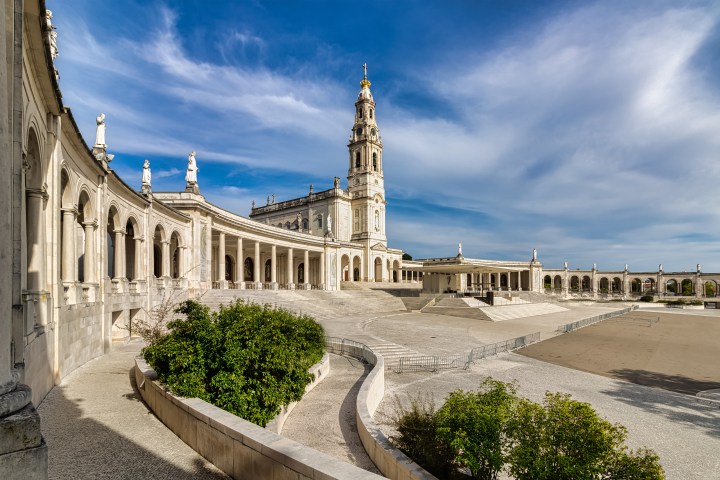 Large neoclassical building with arches and a tall bell tower under a blue sky.