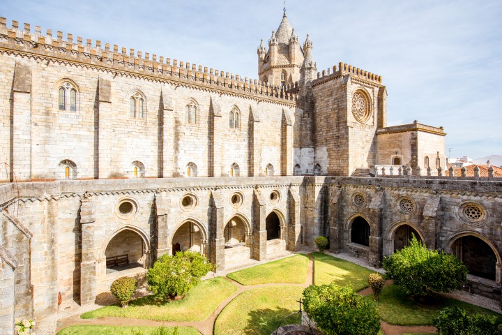 Historic cathedral with arched cloister and grassy courtyard under a clear sky.