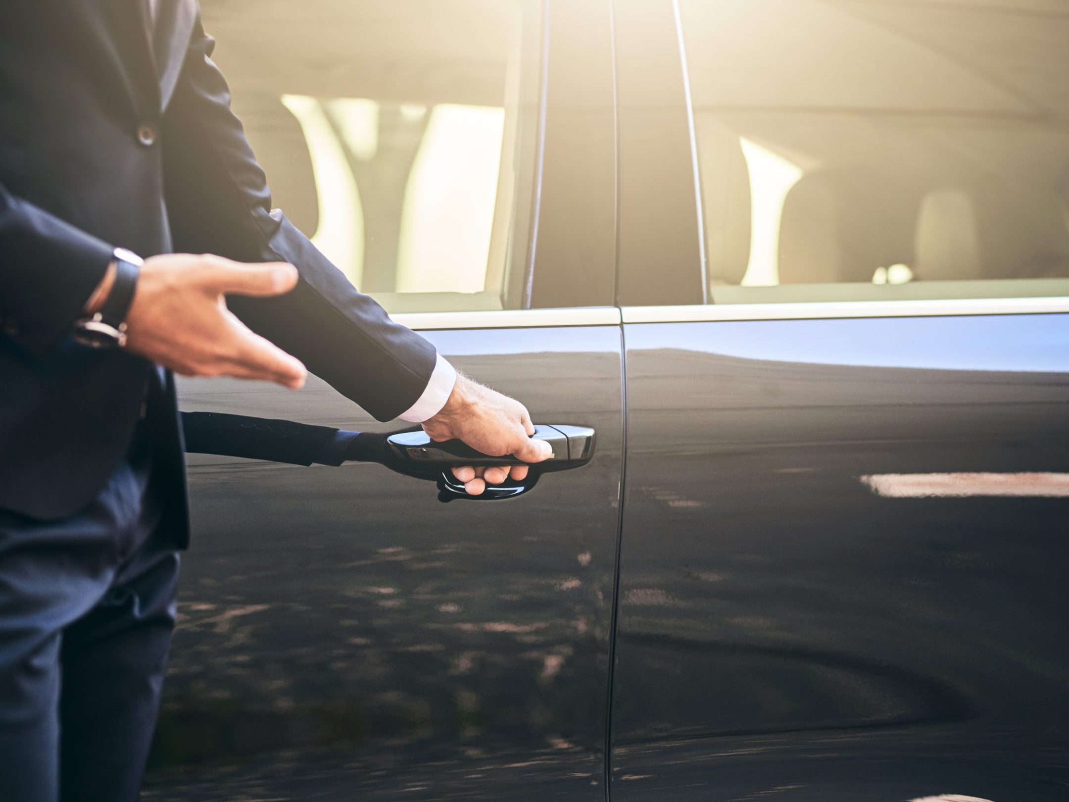 Person in suit opening driver's side door of a luxury car.